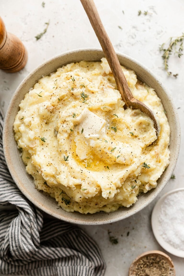 Overhead view of a bowl of freshly mash potatoes topped with fresh herbs and melted butter.