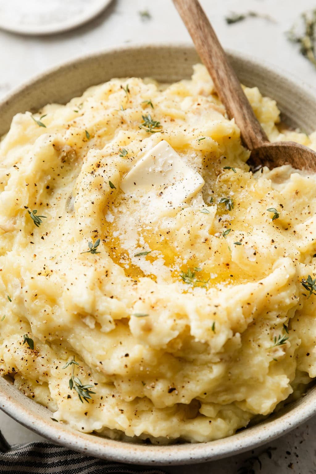 Close up view of a bowl of mashed potatoes topped with fresh herbs, black pepper, and melted butter. 