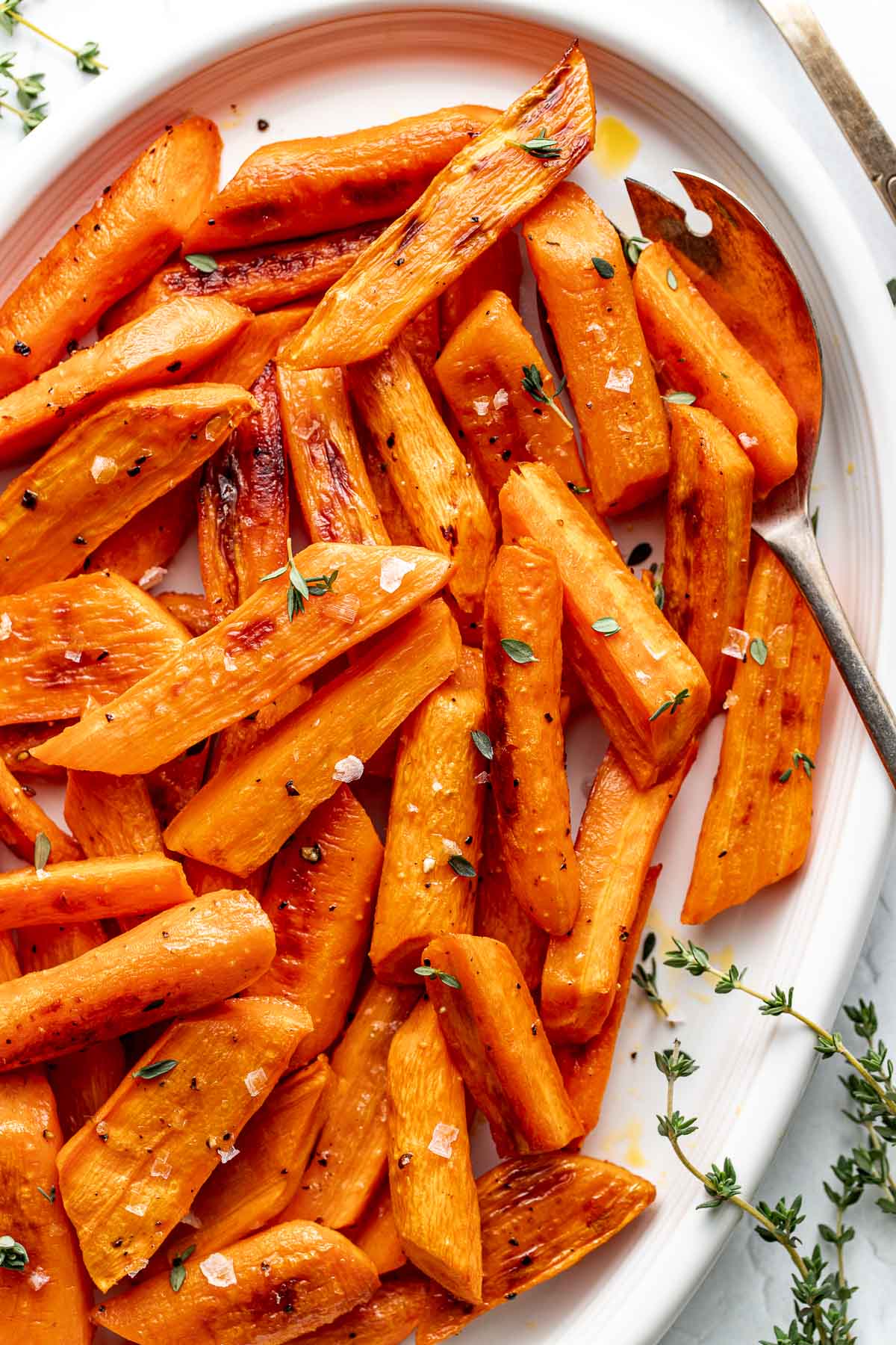Close up view of a platter filled with freshly roasted carrots topped with flakey sea salt and fresh herbs.
