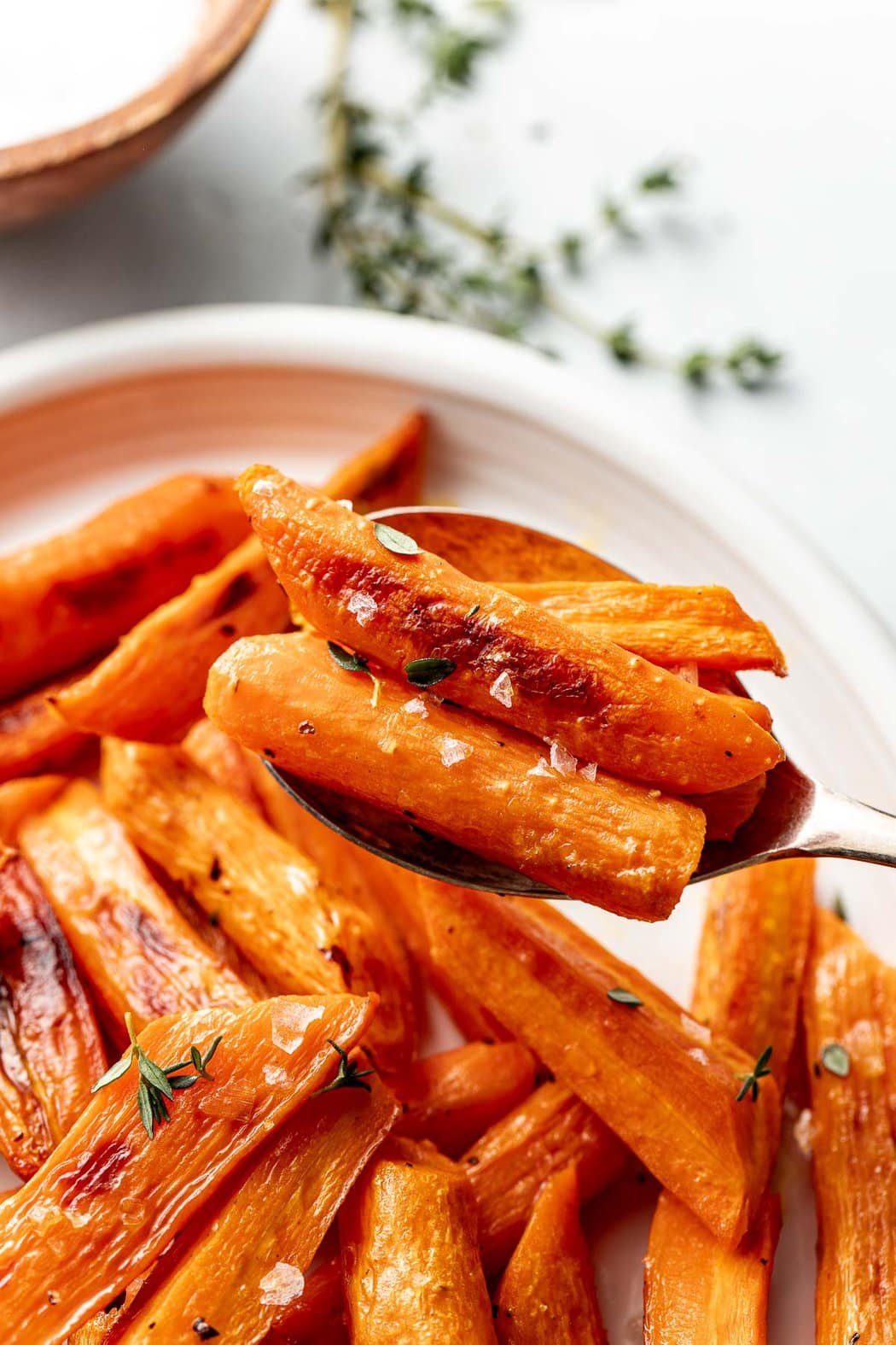 Close up view of a spoon filled with freshly roasted carrots sprinkled with flakey sea salt and fresh herbs.