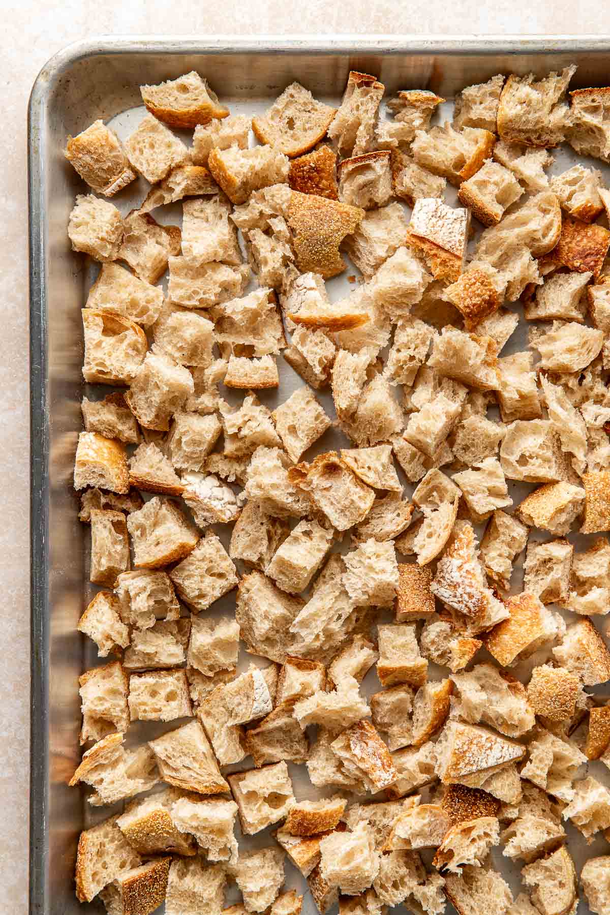 Overhead view of a sheet pan filled with cubes of bread pieces spread evenly.