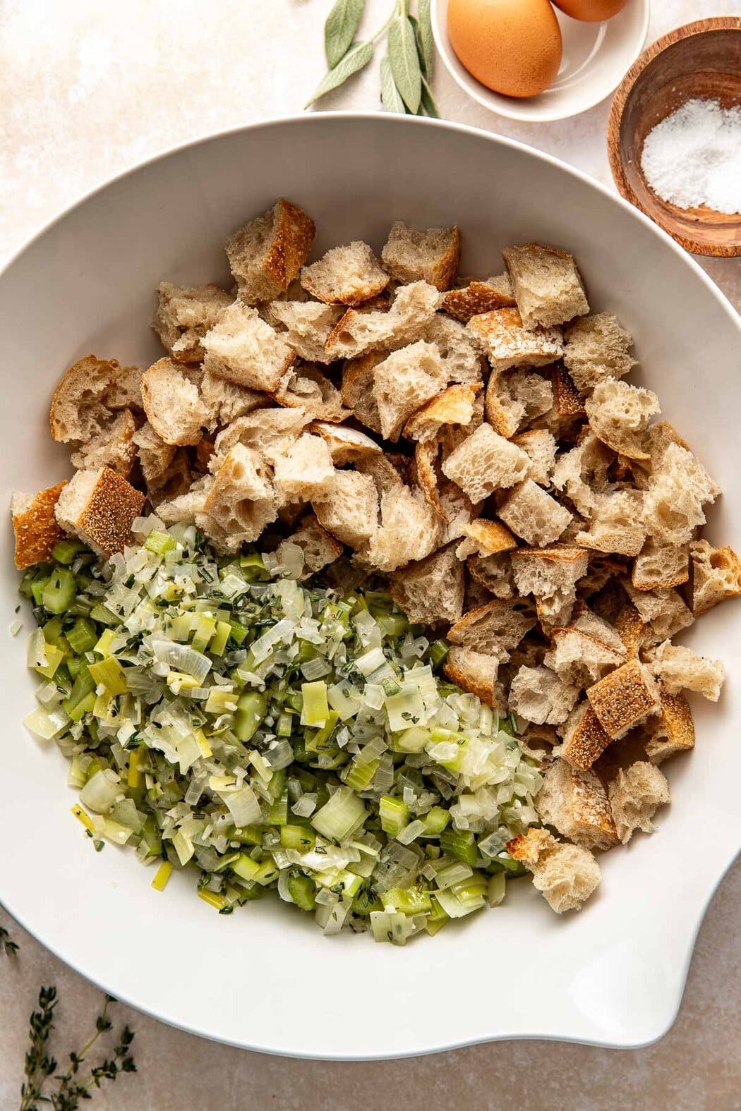 Overhead view of a white bowl filled with bread cubes and sauteed onions and celery ready for combining.