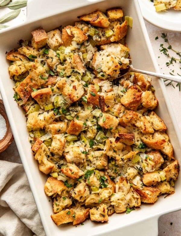 Overhead view of a white baking dish filled with freshly roasted stuffing with herbs sprinkled on top.