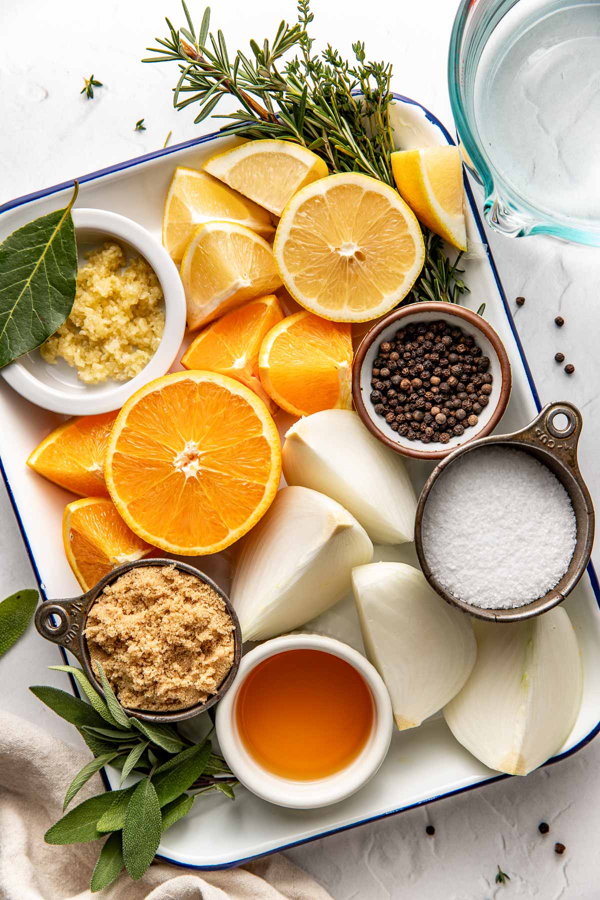Overhead view of a platter filled with Turkey Brine ingredients including sliced lemons, onions, and fresh herbs. 