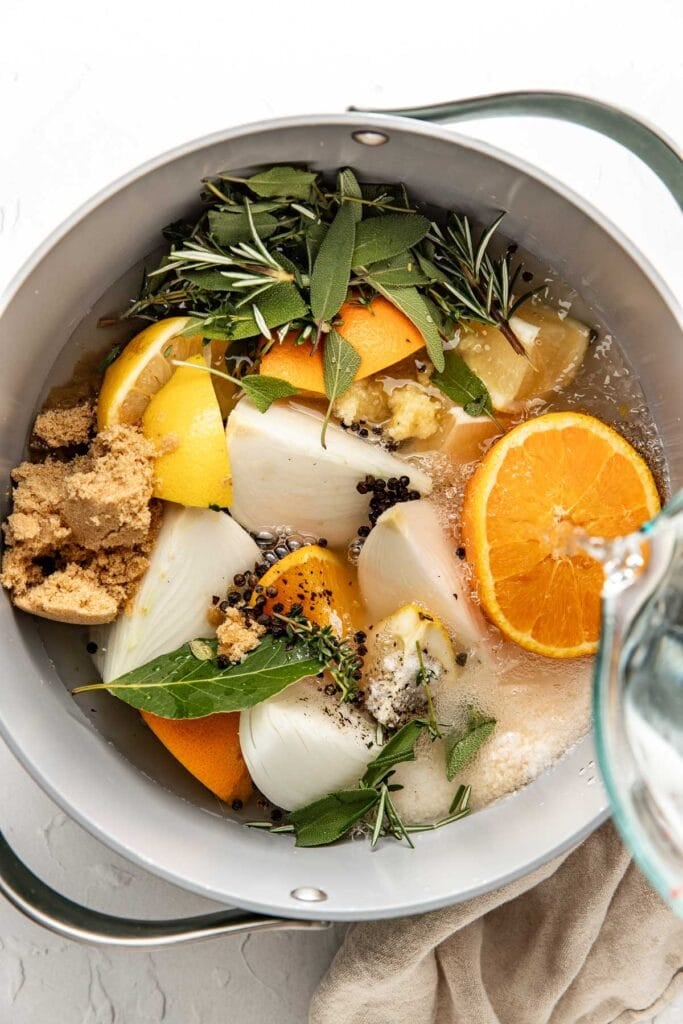 Overhead view of a large pot filled with Turkey Brine ingredients with water being poured over the top. 