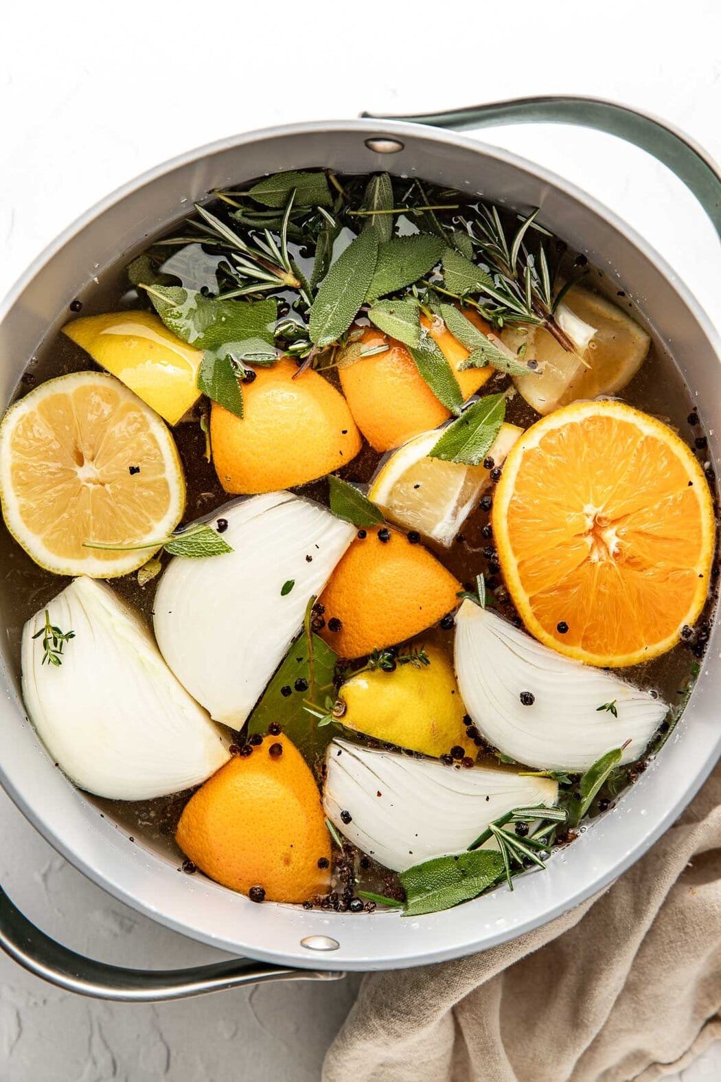 Overhead view of a large pot filled with Turkey Brine ingredients including slices lemons, onions, and fresh herbs. 