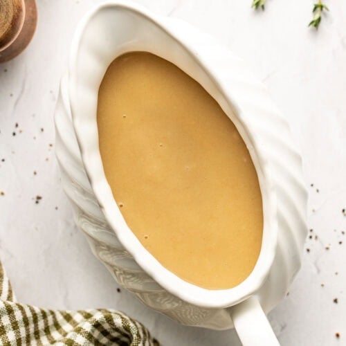 Overhead view of a white gravy boat filled with turkey gravy on a marble countertop with a plaid towel on the side.