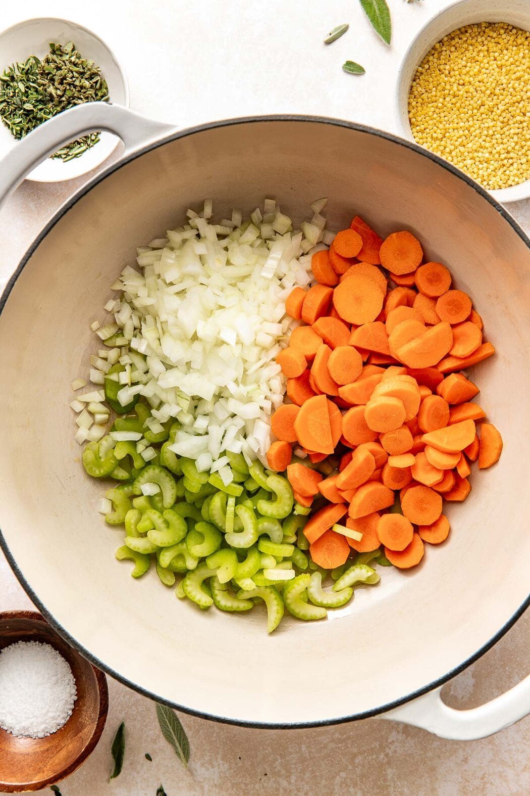 Overhead view of a Dutch oven filled with chopped carrots, celery, and onions ready for sautéing. 