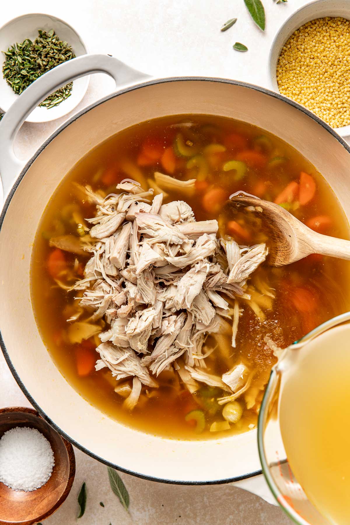 Overhead view of a Dutch oven filled with turkey soup with broth being poured into the mixture. 