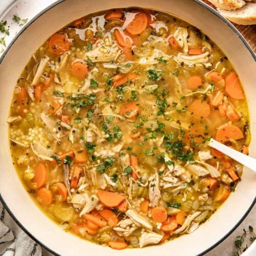 Overhead view of a Dutch oven filled with turkey soup topped with fresh herbs and black pepper.