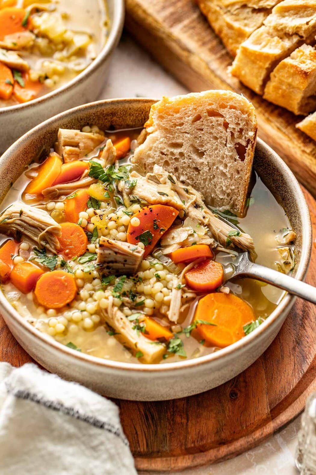 Close up view of a bowl of Turkey Soup with a piece of sourdough bread stuck in the side of the bowl. 