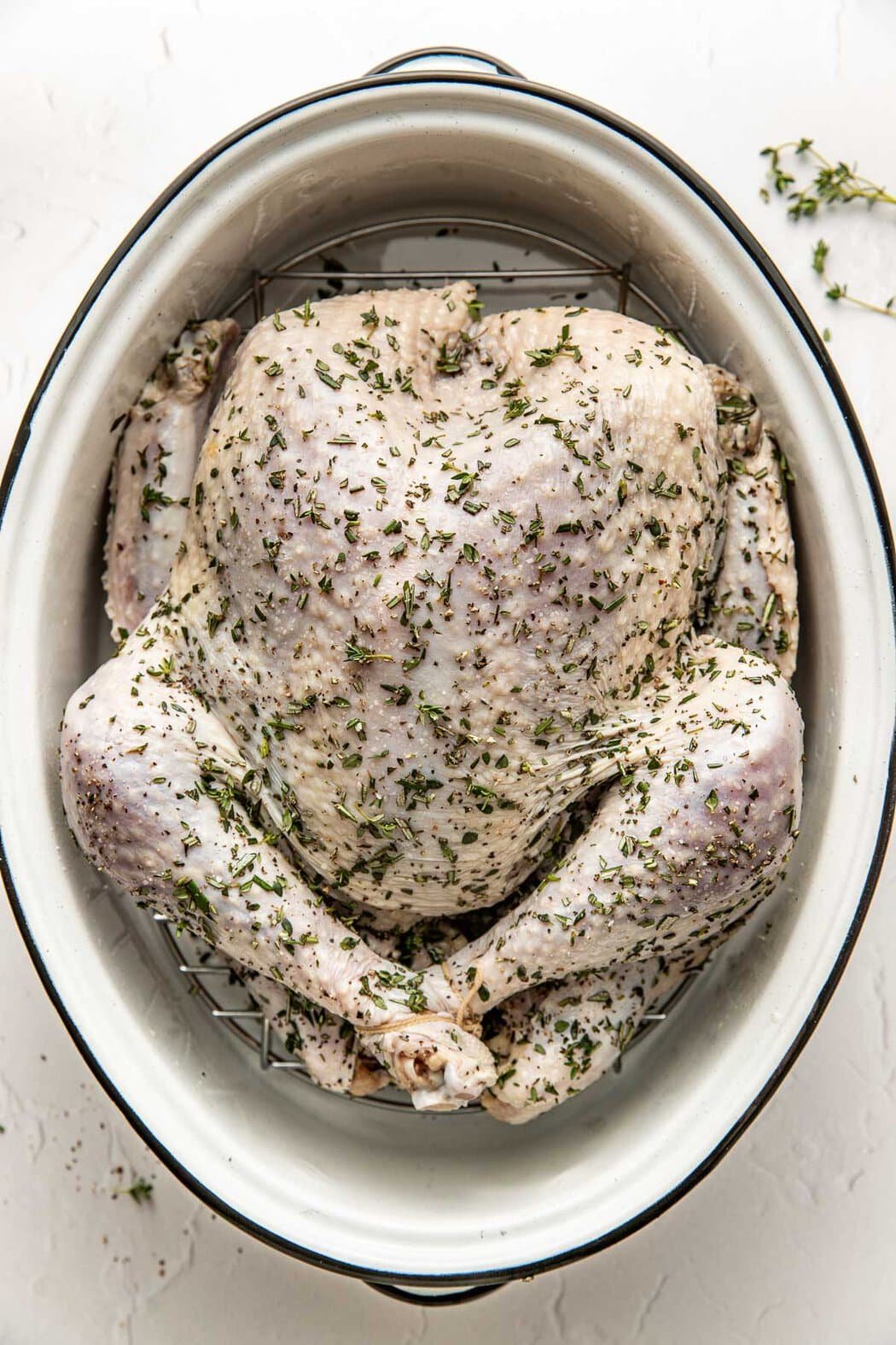Overhead view of a seasoned turkey in a white roasting pan ready for the oven. 