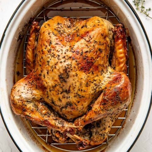 Overhead view of a freshly roasted turkey in a white roasting pan on a wire rack surrounded by drippings.