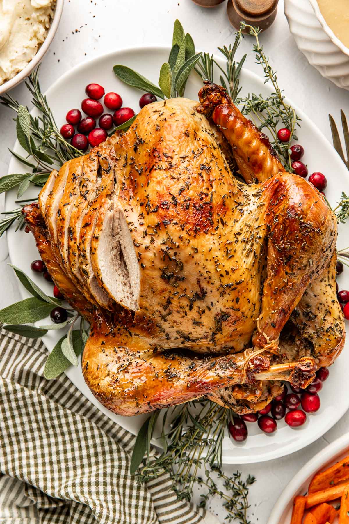 Close up view of a freshly roasted turkey that is laying on a platter with fresh herbs and cranberries surrounding it. 