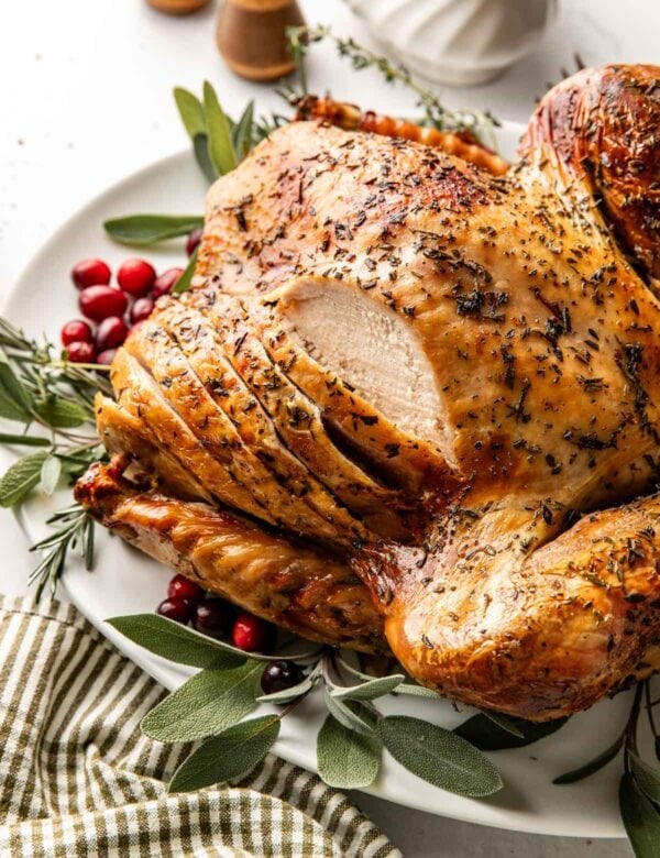 Side view of a whole roasted turkey on a platter with fresh cranberries and herbs all around it