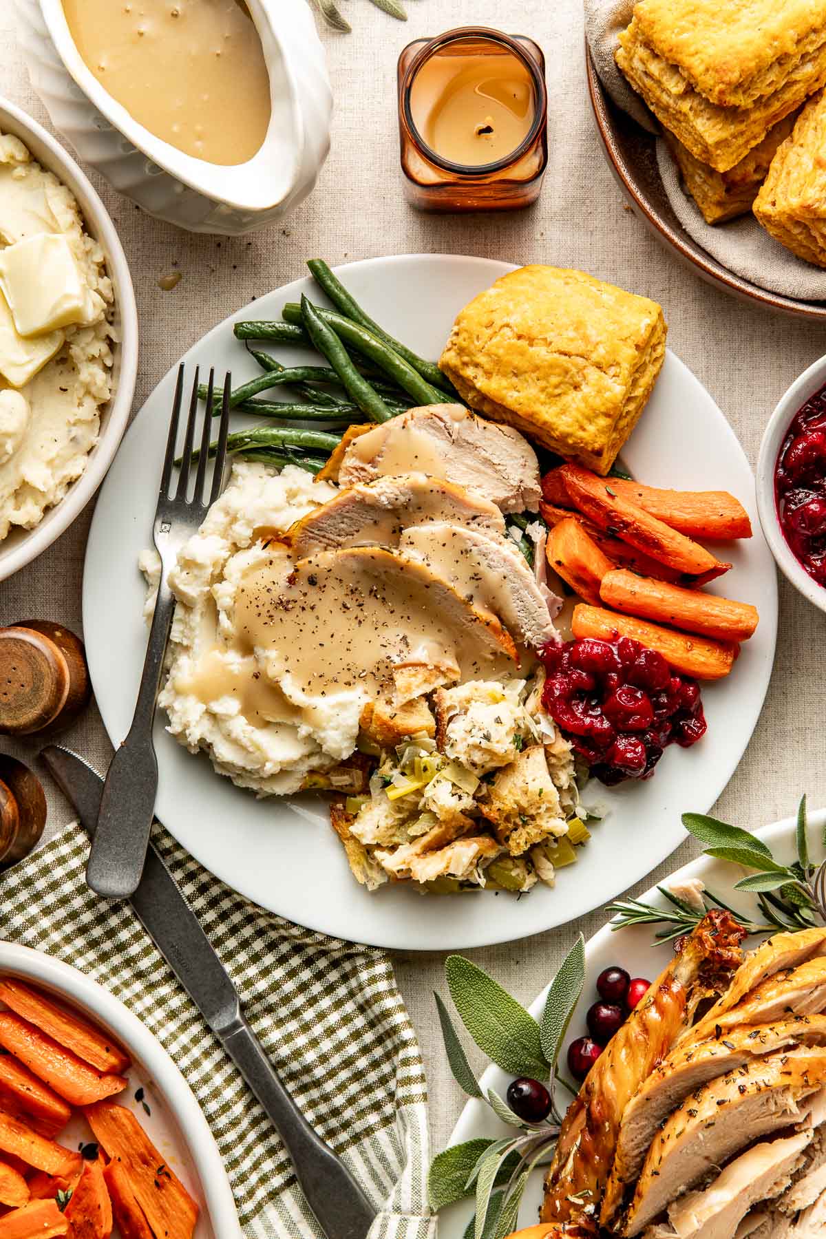 Overhead view of a thanksgiving table including a plate filled with mashed potatoes and stuffing topped with sliced turkey and drizzled with gravy. 