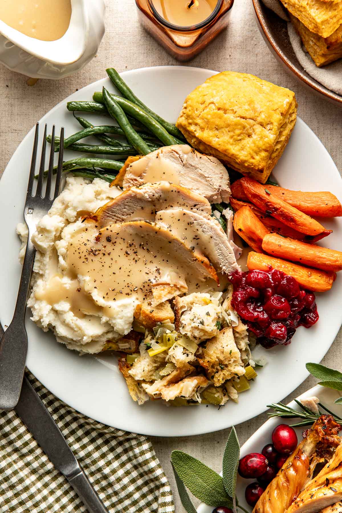Overhead view of a white plate filled with a variety of classic thanksgiving foods including sliced turkey with gravy drizzled over the top. 
