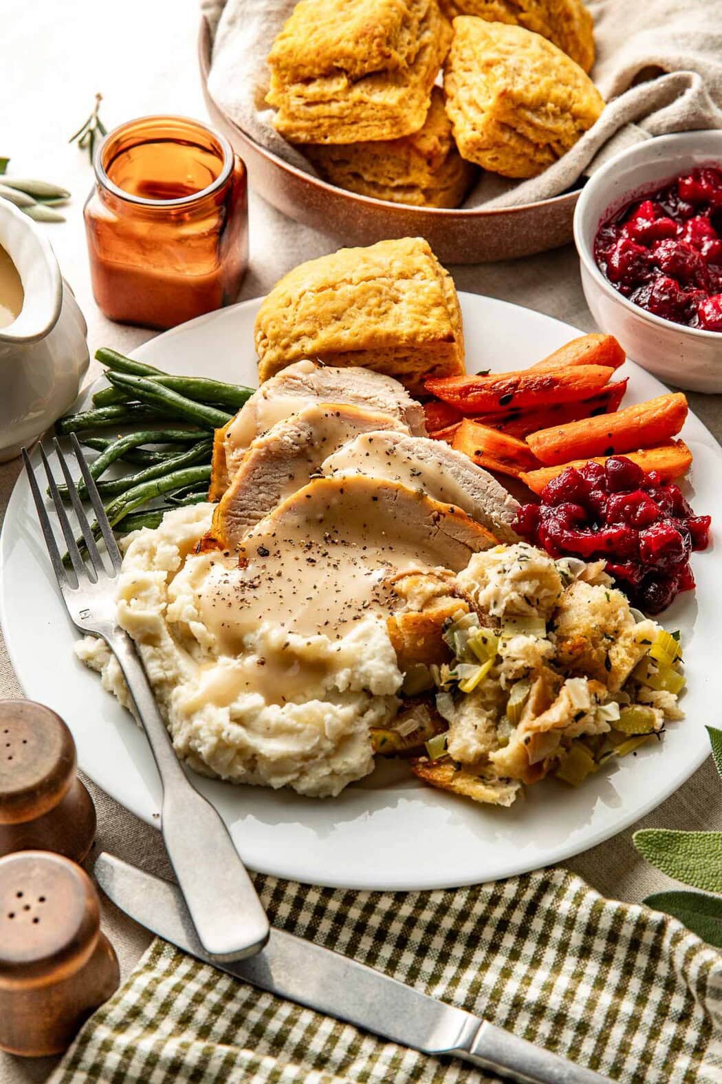 Close up view of a thanksgiving table filled with a variety of foods including a plate with sliced turkey drizzled with gravy and sprinkled with black pepper. 