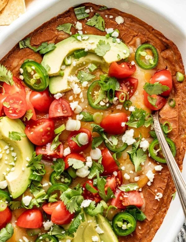 Close up overhead view of homemade bean dip in a dish topped with avocado slices, tomatoes, and jalapeno slices