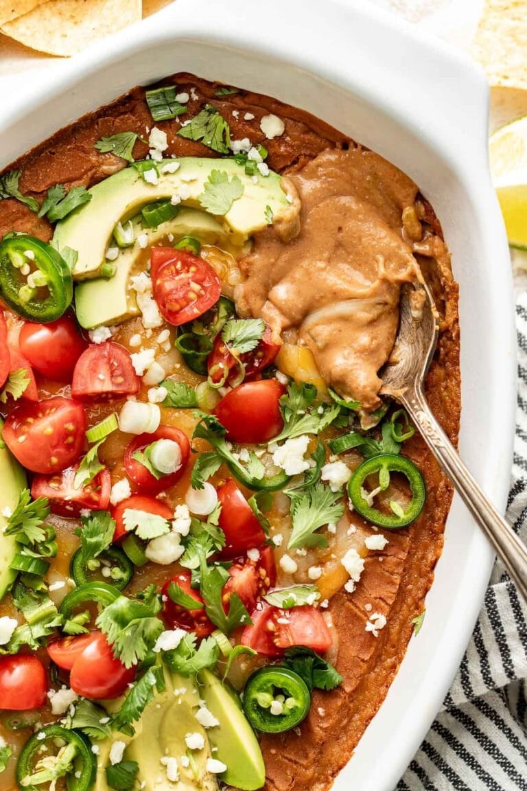 Overhead view of an oval baking dish filled with bean dip and topped with avocado, jalapeno, and diced tomatoes.