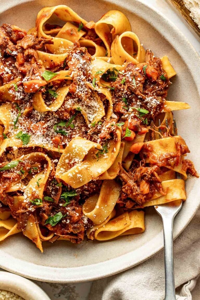 Close up view of a plate of Oven-Braised Beef Ragu topped with parmesan cheese and fresh herbs.