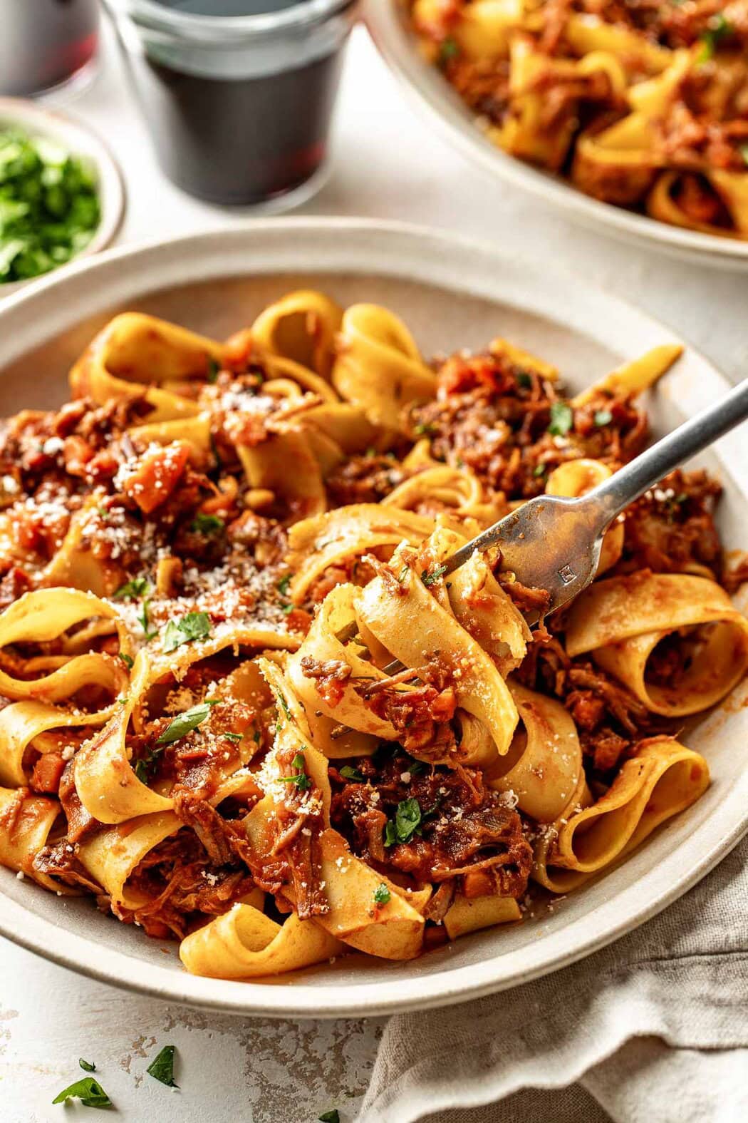 Close up view of a plate of Oven-Braised Beef Ragu and a fork scooping up a section of the noodles.