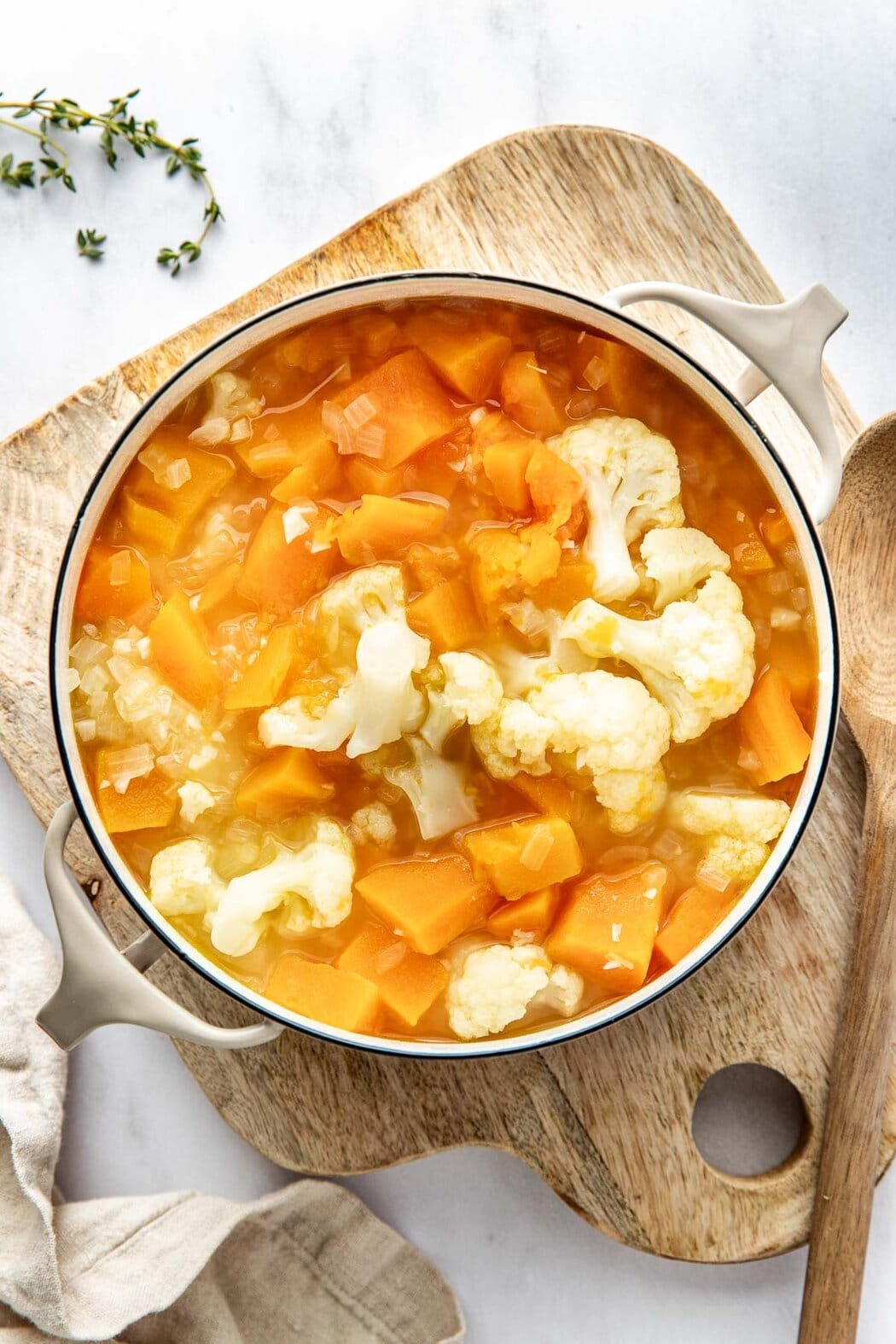 Overhead view of a pot filled with cubed butternut squash and cauliflower pieces in water.