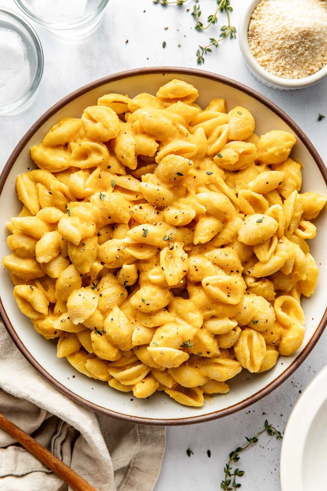 Overhead view of a ceramic white bowl filled with Butternut Squash Mac and Cheese sprinkled with black pepper and fresh herbs. 