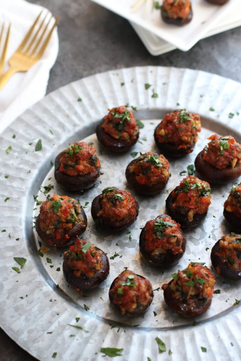 Close up view of a plate of chorizo stuffed mushrooms topped with fresh herbs.