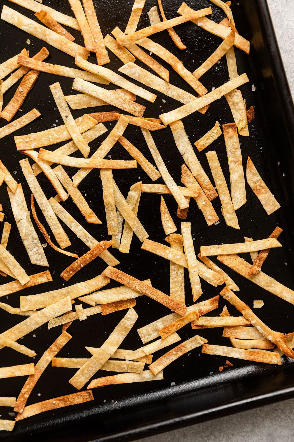 Close up view of a sheet pan filled with thin tortilla strips.