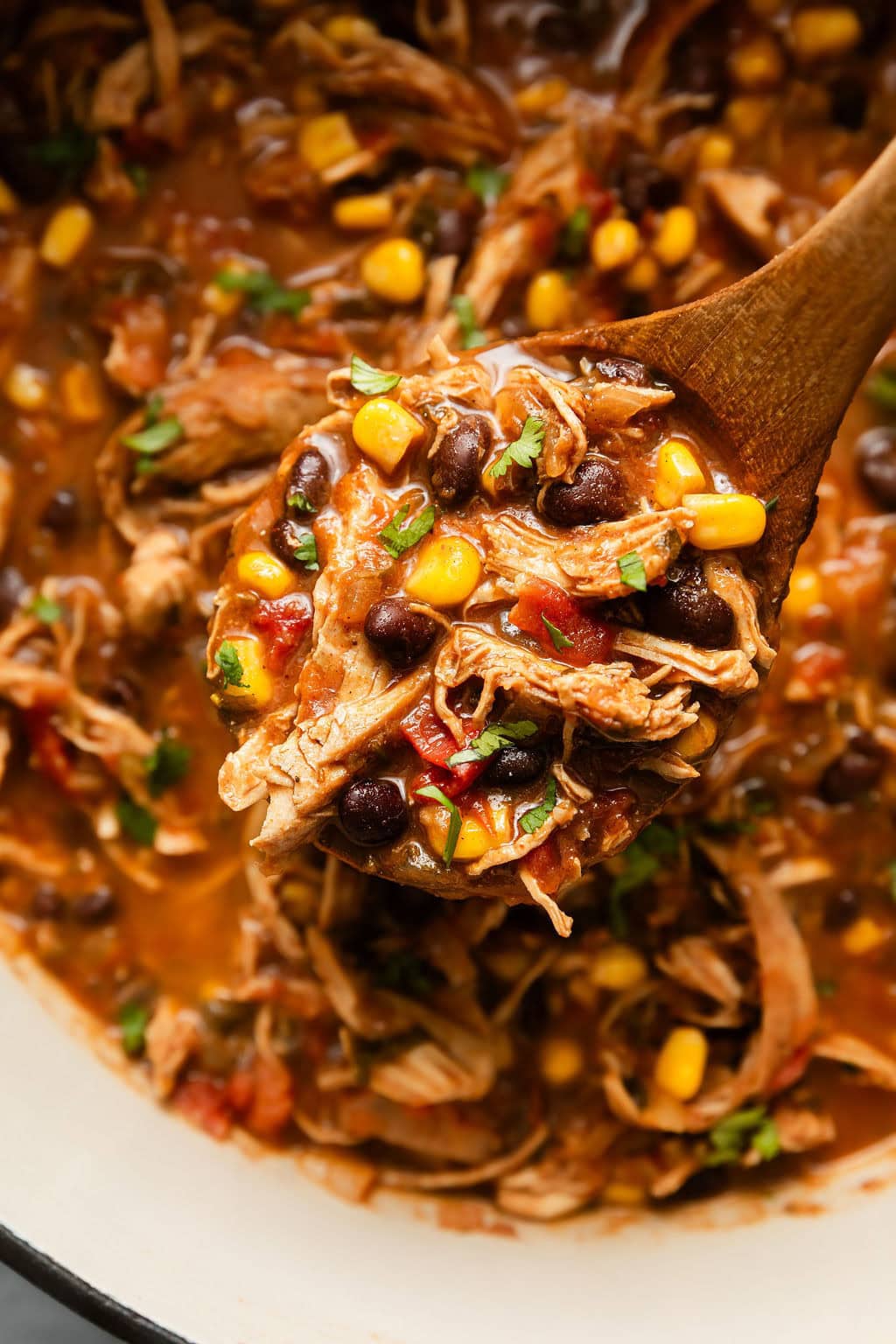 Close up view of a wooden spoon bringing a scoop of Chicken Tortilla Soup out of the pot.