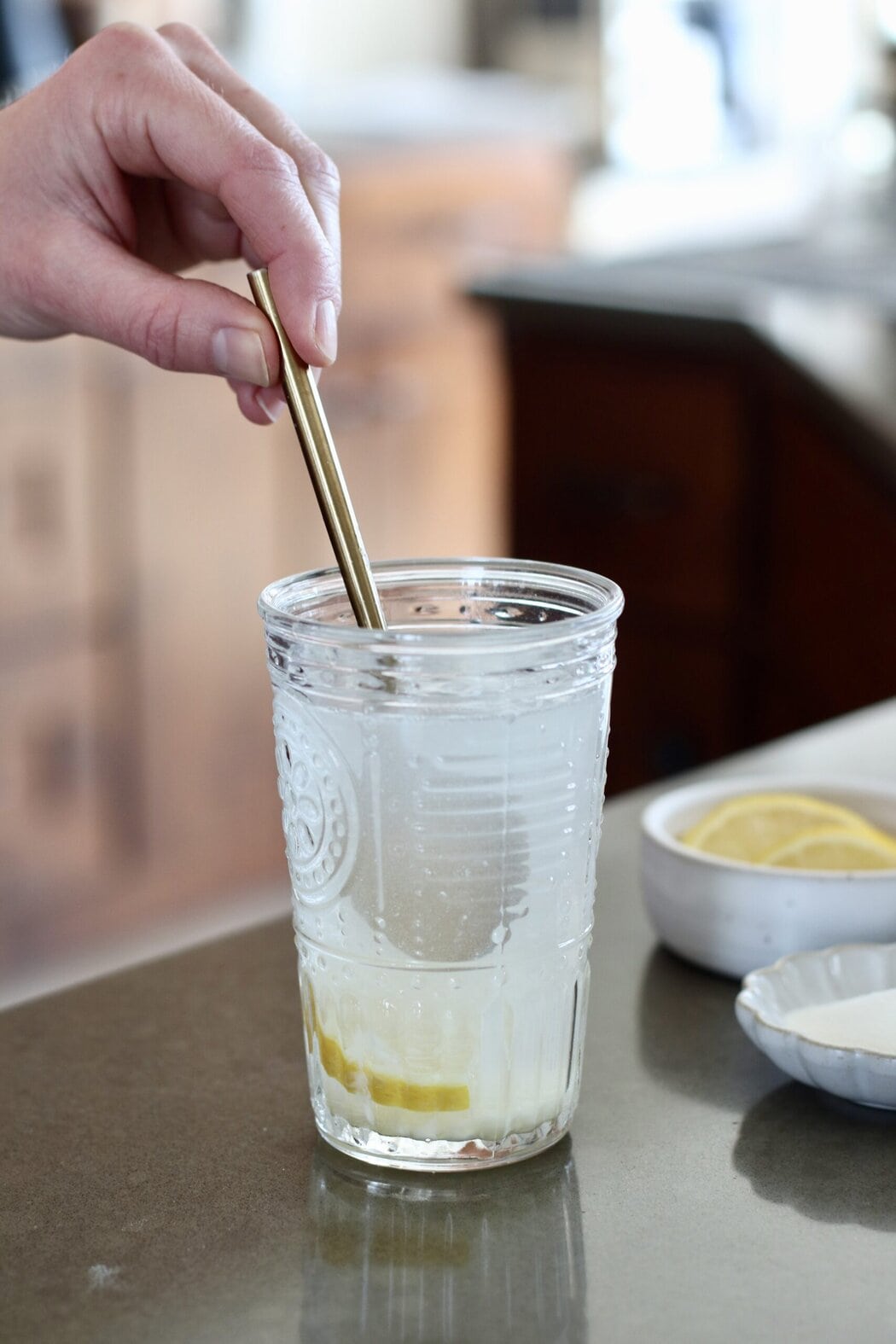 Close up view of a glass of water with lemon and collagen in it being stirred with a metal spoon.