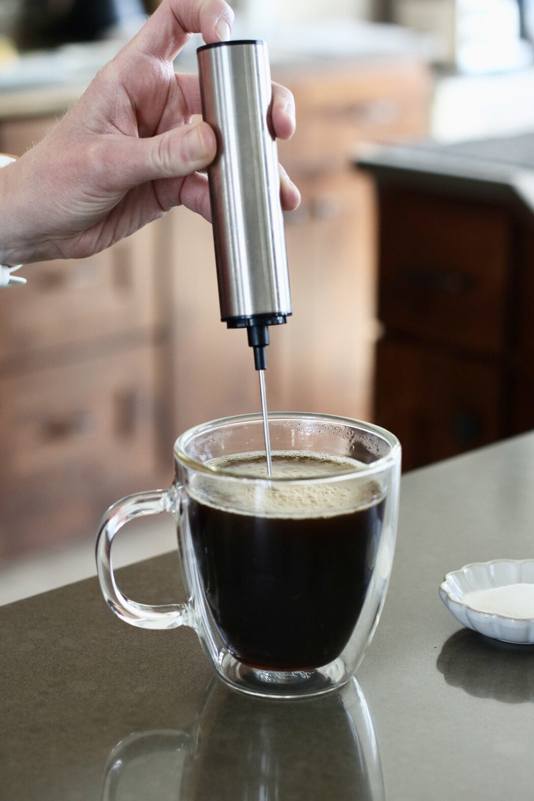 Close up view of a hand holding a frother in a cup of coffee.