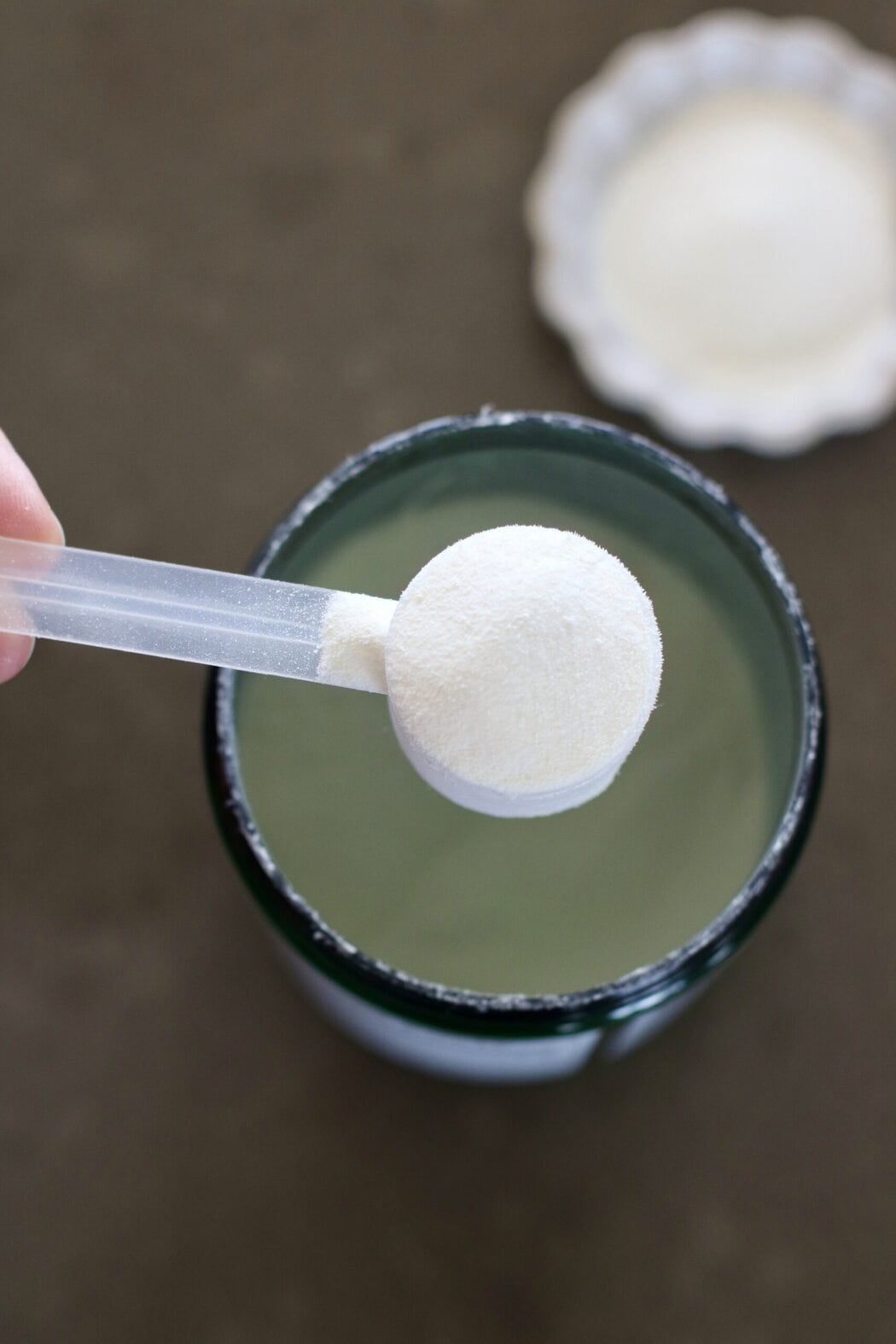 Overhead view of a hand bringing up a scoop of collagen out of a canister.