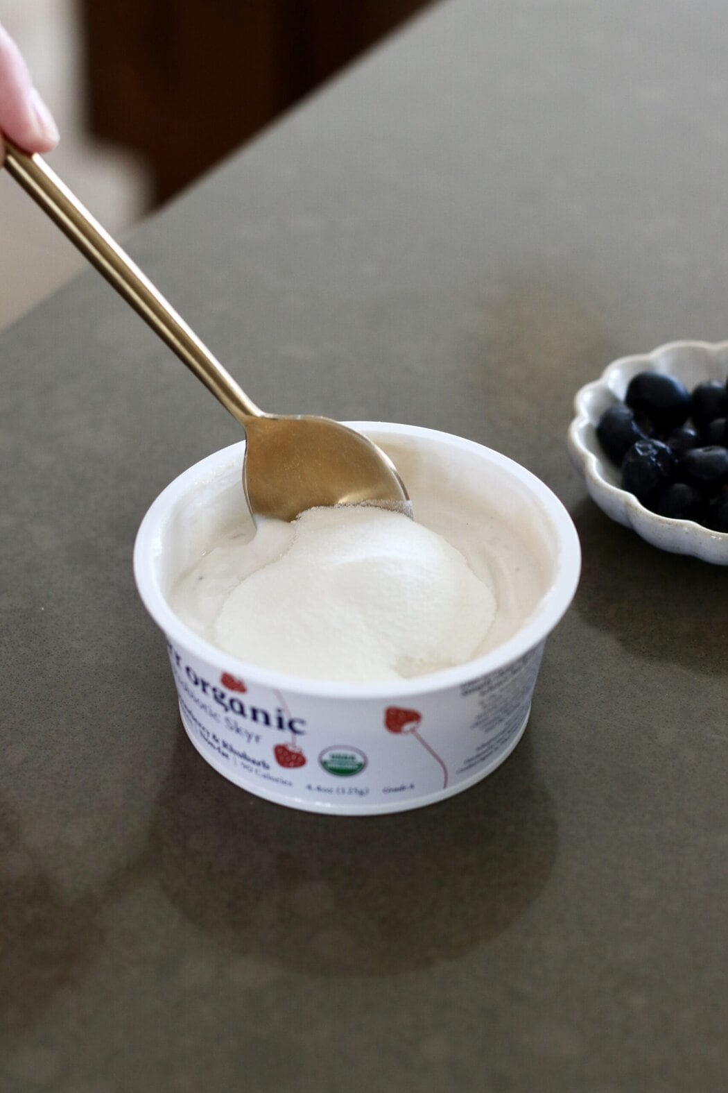 Close up view of a yogurt cup sprinkled with collagen on top with a metal spoon in the cup.