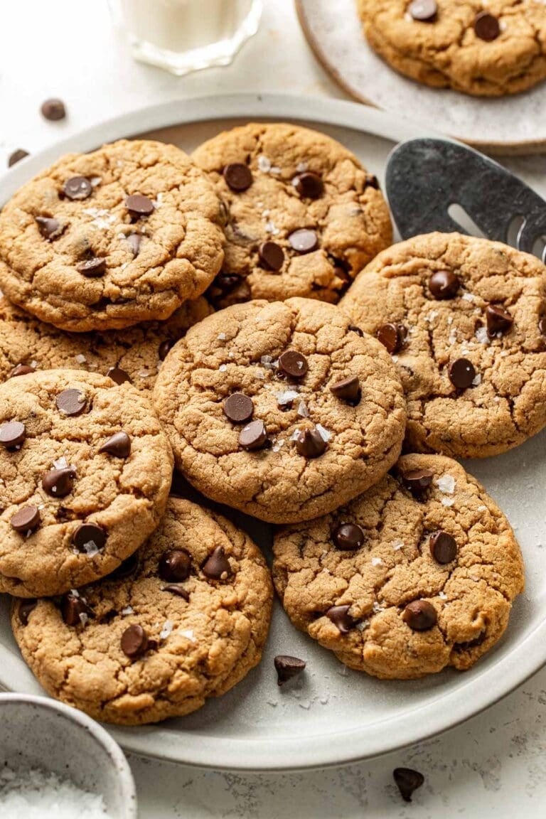 Overhead view of a plate filled with chocolate chip protein cookies sprinkled with flakey sea salt.