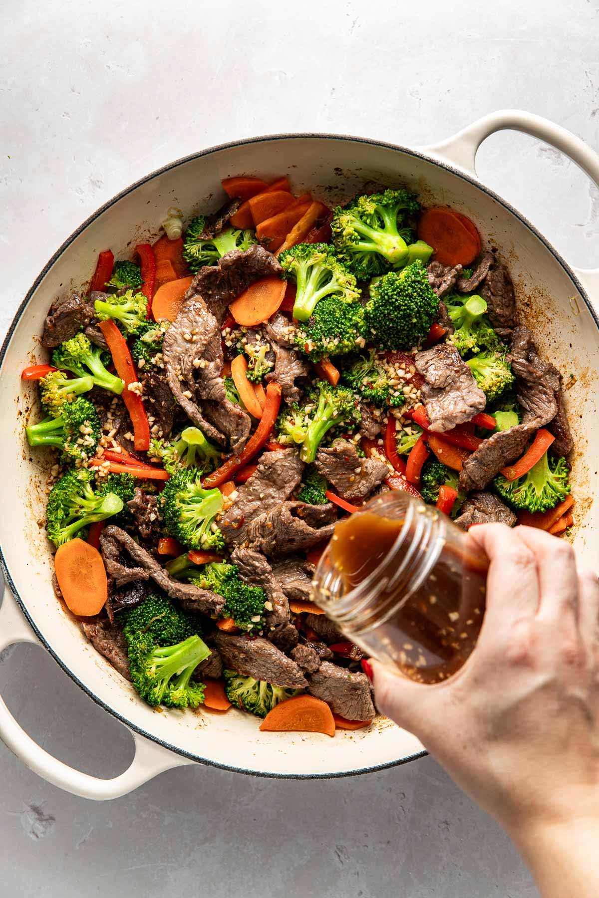 Overhead view of a skillet filled with steak and vegetables and a hand pouring Stir Fry Sauce over the top.