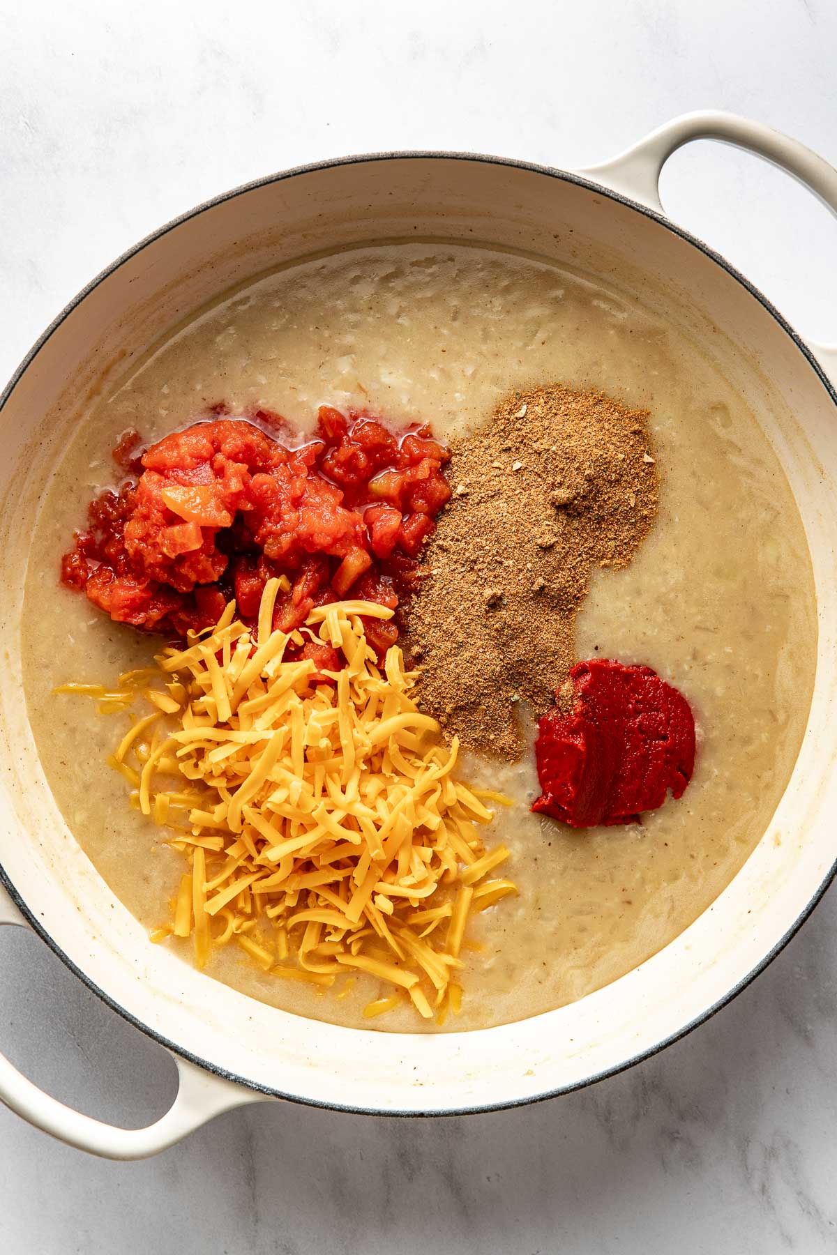 Overhead view of a white skillet filled with shredded cheese, tomatoes, and seasonings ready to be combined.