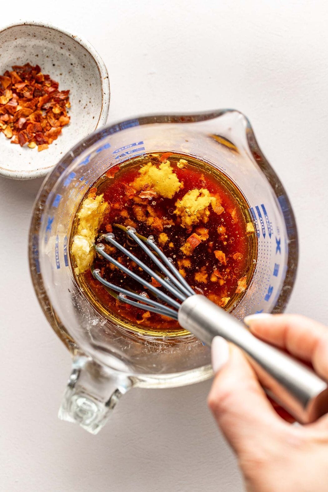 Overhead view of a glass measuring cup filled with Asian Salad Dressing and a hand whisking the liquid.