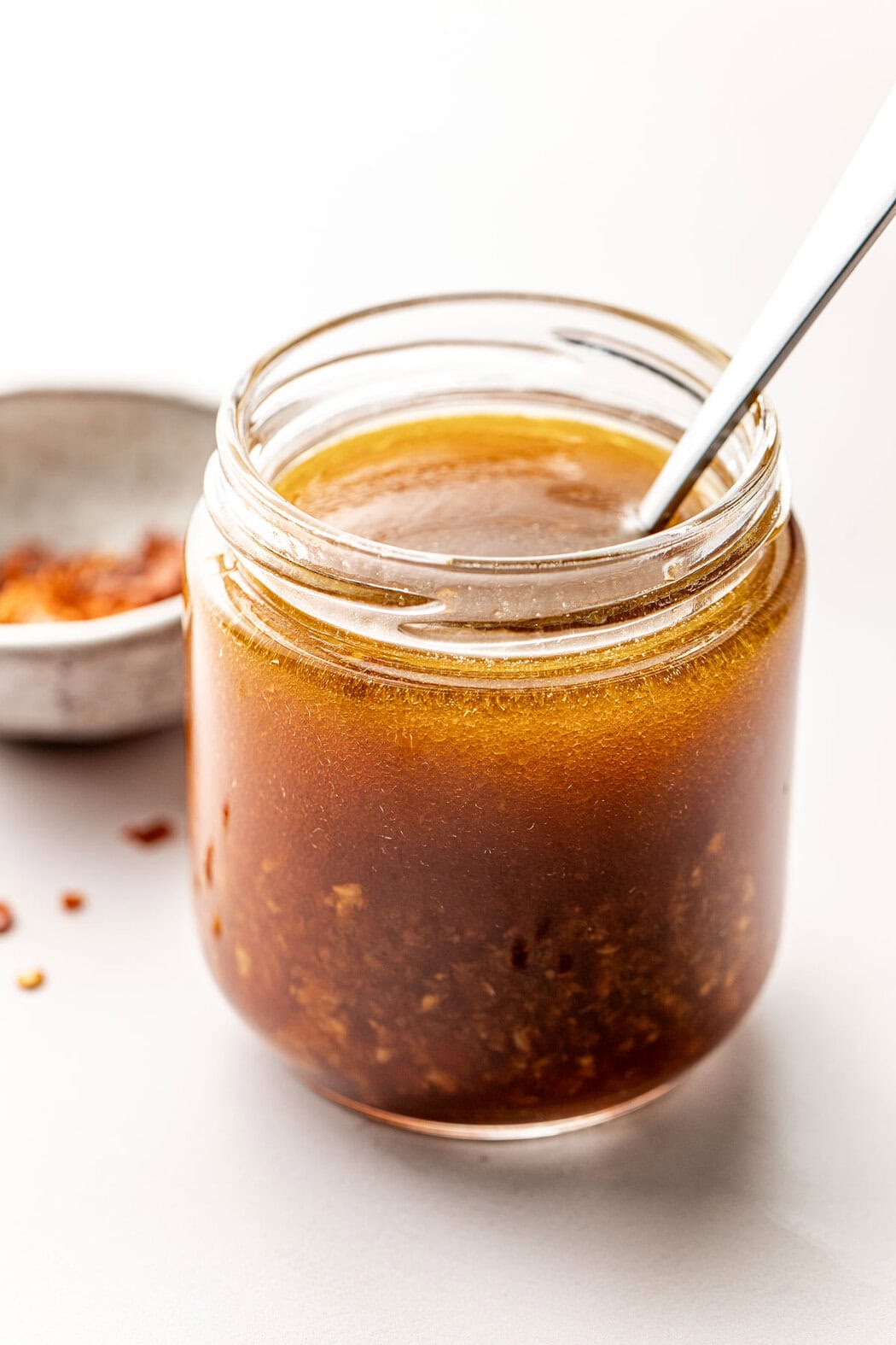 Close up view of a glass jar of Asian Salad Dressing with a spoon stuck into the jar. 
