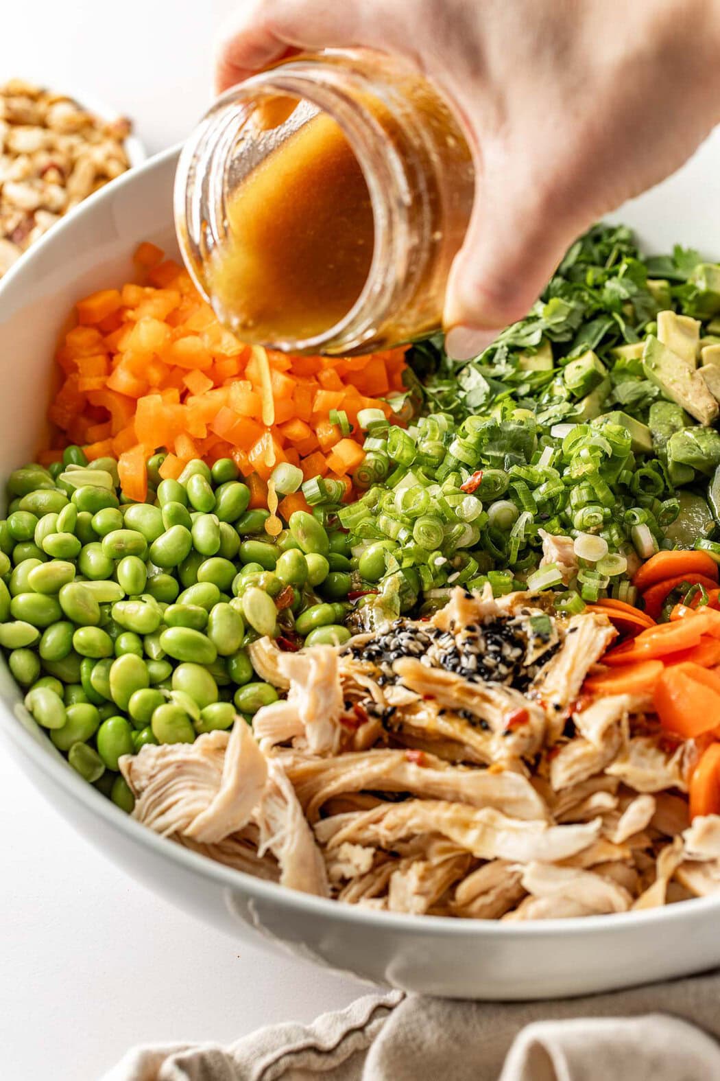 Close up view of a Thai Chicken Salad with a hand pouring dressing over the top from a glass jar.