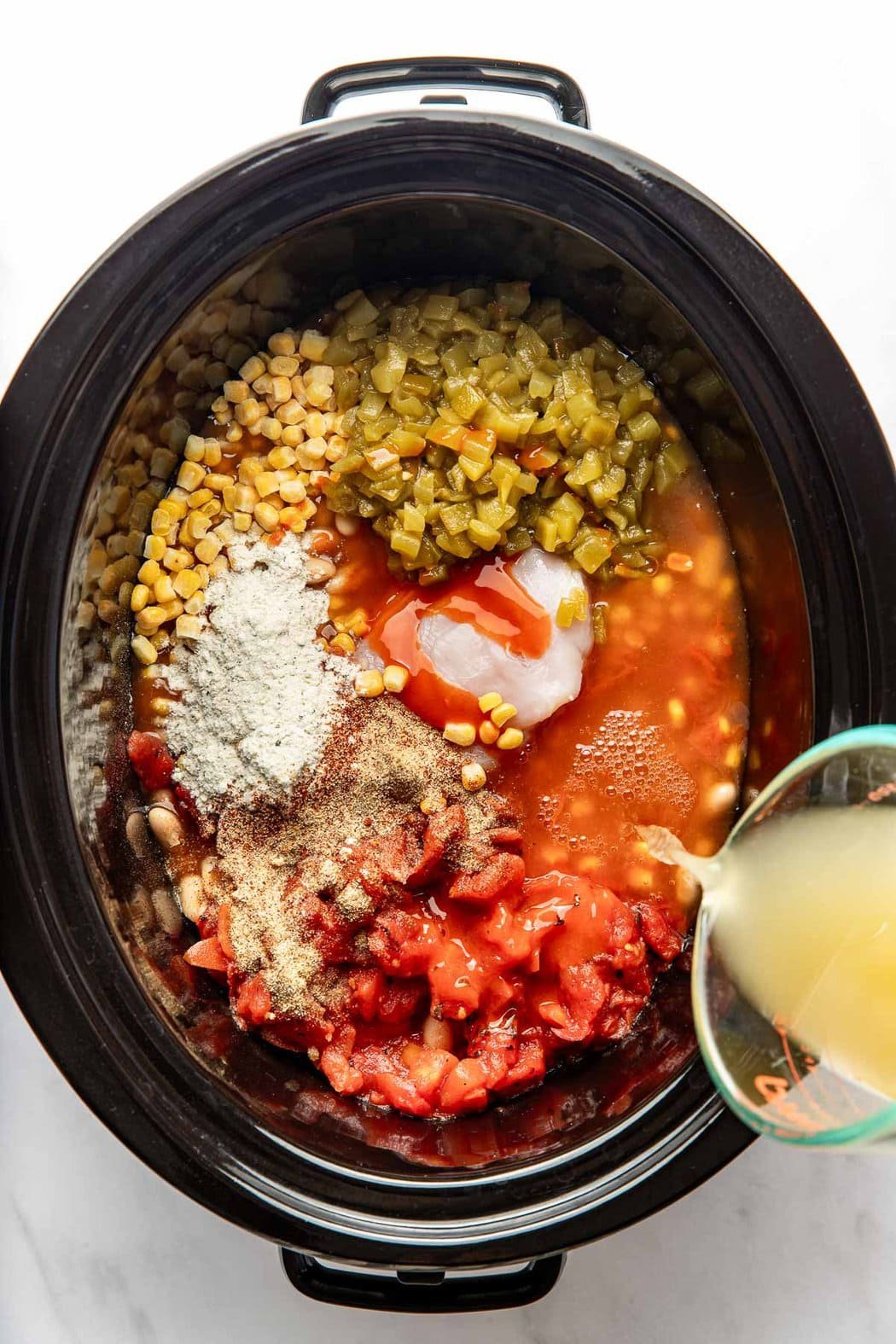 Overhead view of a slow cooker filled with Buffalo Chicken Chili ingredients ready for cooking.