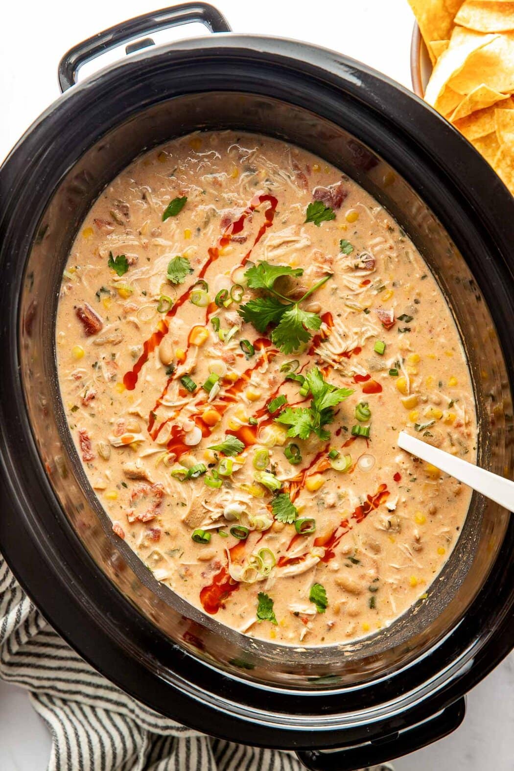 Overhead view of a slow cooker filled with Buffalo Chicken Chili topped with fresh cilantro and drizzled with buffalo sauce.