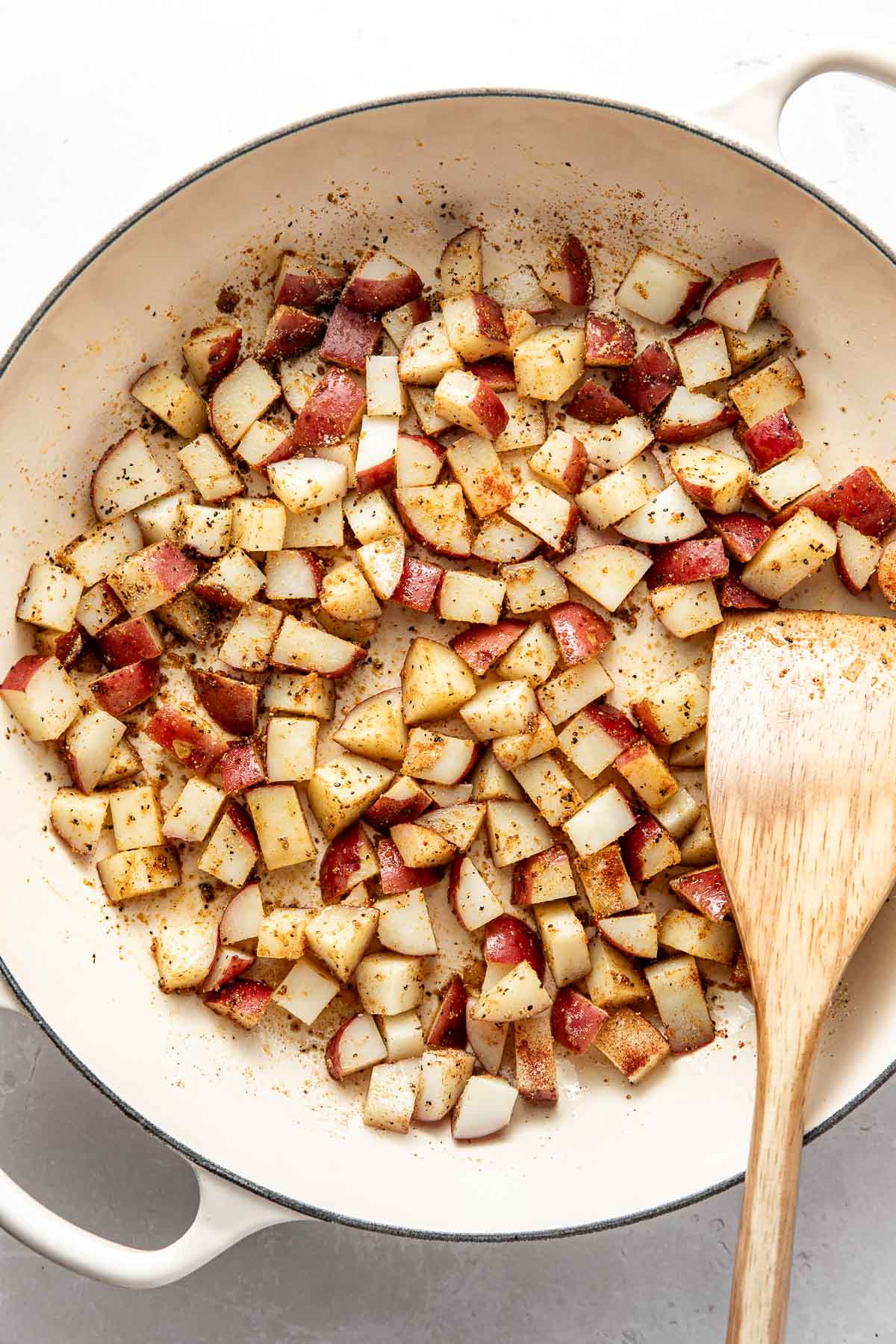 Overhead view of a white skillet filled with diced and sauteed potatoes topped with seasonings.