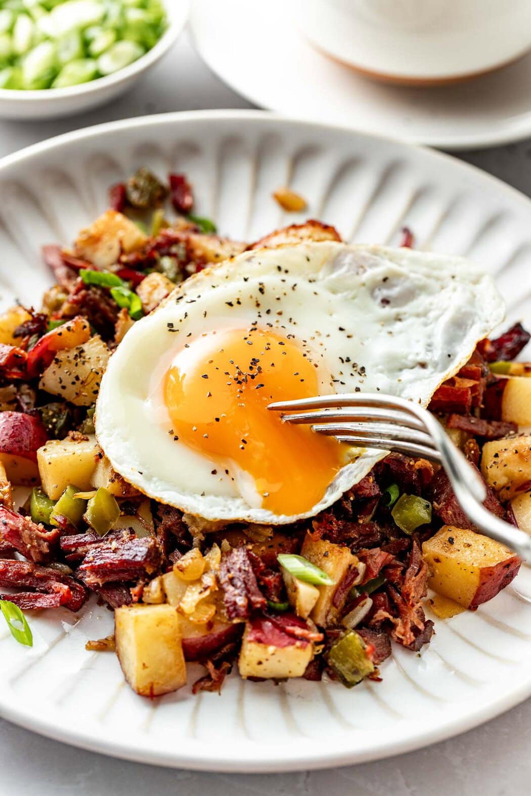 Close up view of a plate of Corned Beef Hash topped with a sunny side up egg sprinkled with pepper.