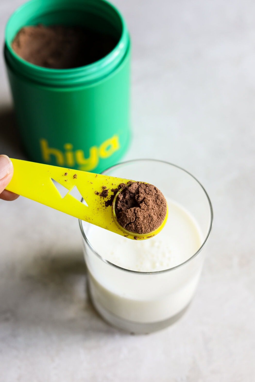 Overhead view of a scoop of hiya chocolate drink powder over a glass of milk on a marble countertop.