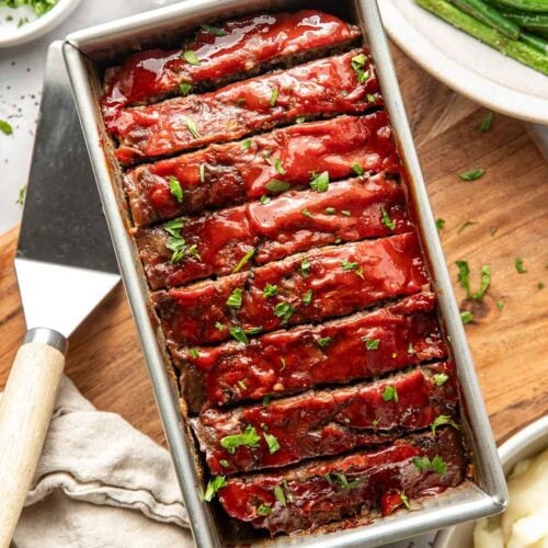 Overhead view of a loaf pan filled with freshly baked meat loaf topped with a tomato topping and sliced for serving.