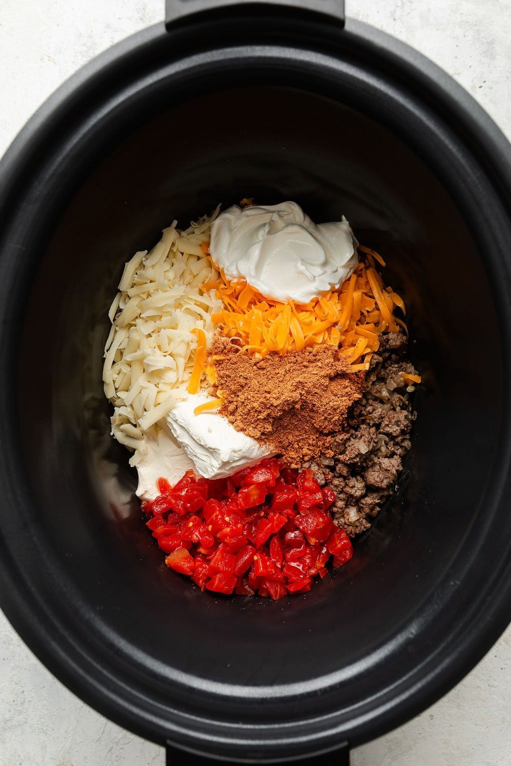 Overhead view of a slow cooker filled with Rotel Dip ingredients arranged in sections of the dish.