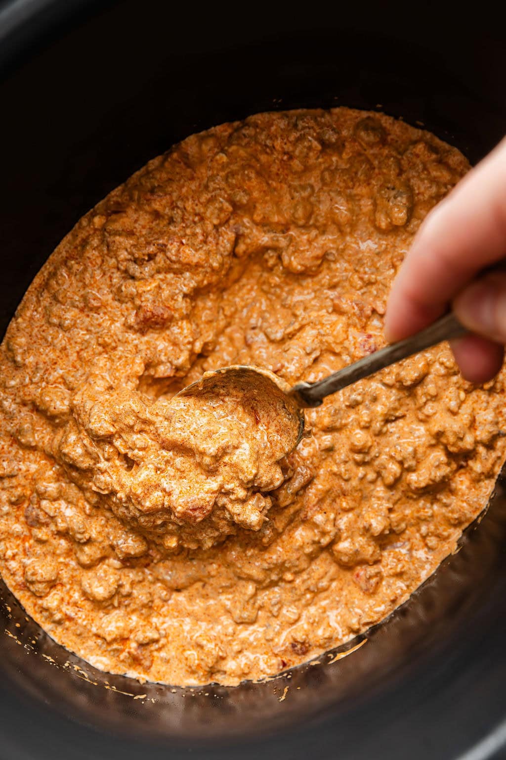 Overhead view of a slow cooker filled with melty rotel dip being stirred with a metal spoon.