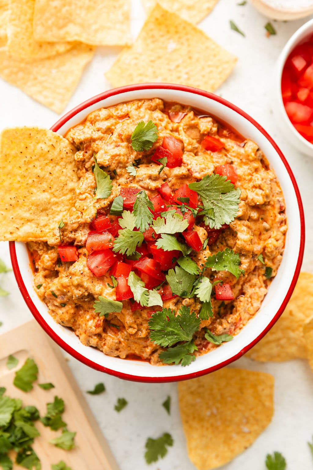 Overhead view of a bowl of rotel dip topped with fresh cilantro and tomato pieces with a tortilla chip stuck into the side.